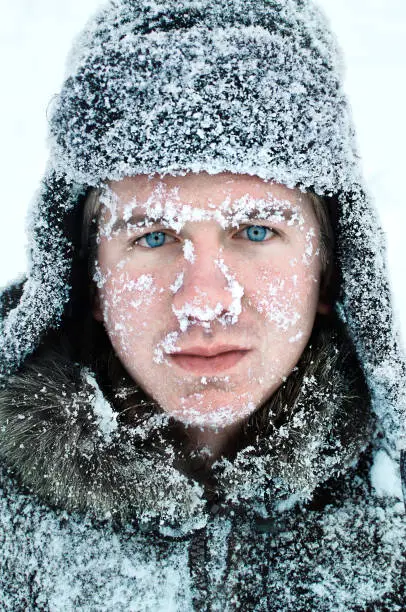 Photo of male face covered with snow with bright blue eyes