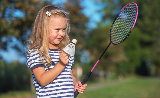Childhood time. Cute little girl playing badminton, having fun in the park