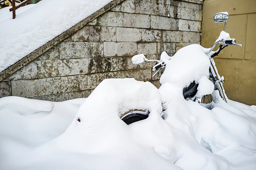 Winter in Russia. Motorcycle parked near the wall of the house is almost completely covered with snow and waiting for spring, and the beginning of the season for long journeys.