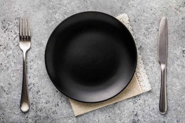 istock Empty ceramic plate in black with a fork and knife on the table, top view 1130350941