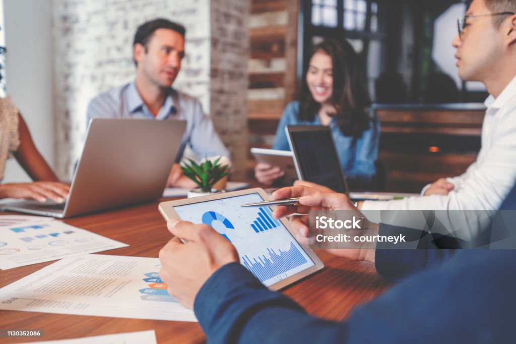 Group of people meeting with technology. Group of people meeting with technology. There are marketing, financial and strategy documents on the wooden board room table and on the computers and digital tablets. Multi ethnic group including Caucasian and African American. Finance Stock Photo