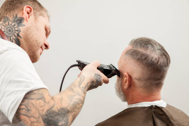 The barber cuts the client- 55 year old gray-haired man