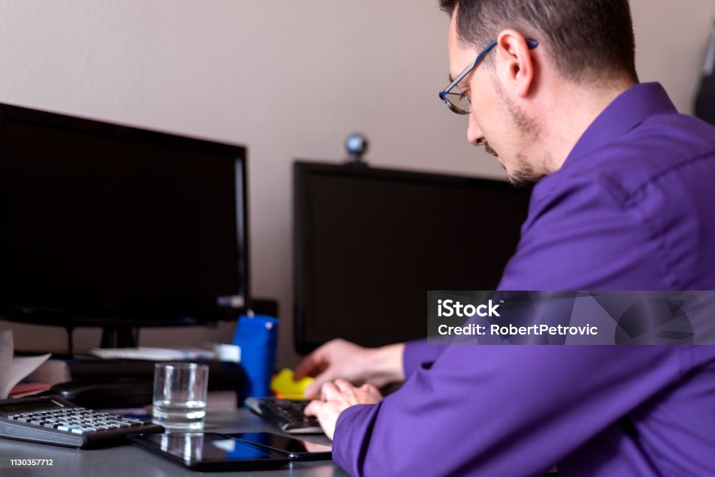 Man at work in office Young businessman in violet shirt sitting at his office desk and looking busy 35-39 Years Stock Photo