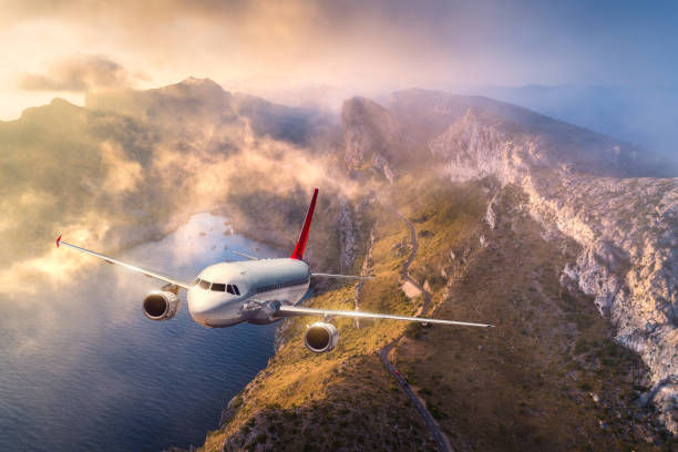 istock Airplane is flying over mountains and low clouds at sunset in summer. Landscape with passenger airplane, sky in clouds, rocks, sea, sunlight. Business travel. Commercial plane. Aerial view of aircraft 1130357885