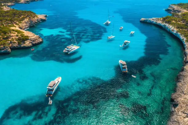 Photo of Aerial view of boats and luxury yachts in transparent sea at sunny day in Mallorca, Spain in summer. Sea coast. Colorful seascape with marina bay, azure water. Top view from drone of shore. Travel