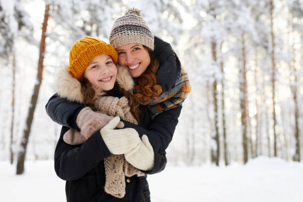 Mother and Girl Posing in Winter Waist up portrait of loving mother embracing cute little girl in winter forest and smiling at camera, copy space kid tripped stock pictures, royalty-free photos & images