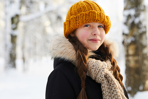 Head and shoulders portrait of smiling teenage girl in winter forest looking at camera, copy space
