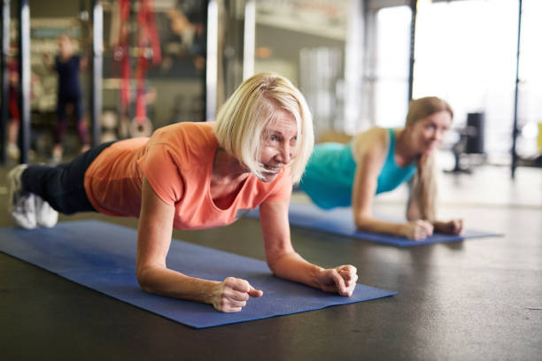 Woman in plank Mature blonde active woman standing in plank on mat during workout in contemporary fitness center bodyweight training stock pictures, royalty-free photos & images