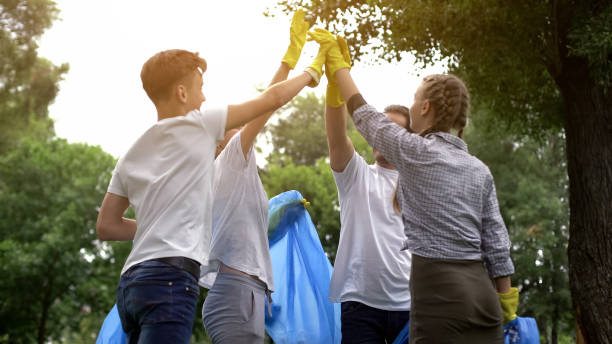 team of volunteers hi-fiving during collecting garbage in park, save nature - wasting time imagens e fotografias de stock