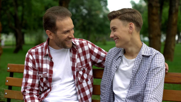 istock Teenage son talking with father on bench, telling secrets and smiling, trust 1130375347