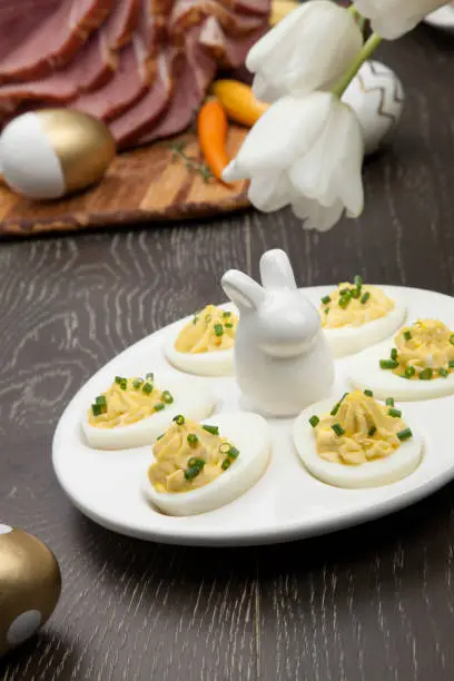 Plate of deviled eggs sidedish for delicious spicey roasted Easter ham dish, asparagus, butternut squash with green peas, baby carrots, strawberries, and Easter decoration.