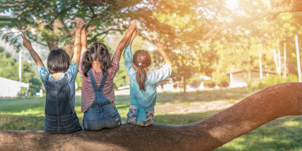 楽しいツリーの下に座って日陰演奏を一緒に楽しんで良い公園のことで幸せな女の子子供と子供たちの友情のコンセプト メモリと学校で友達と学生生活の瞬間時間日 - 少女 ストックフォトと画像