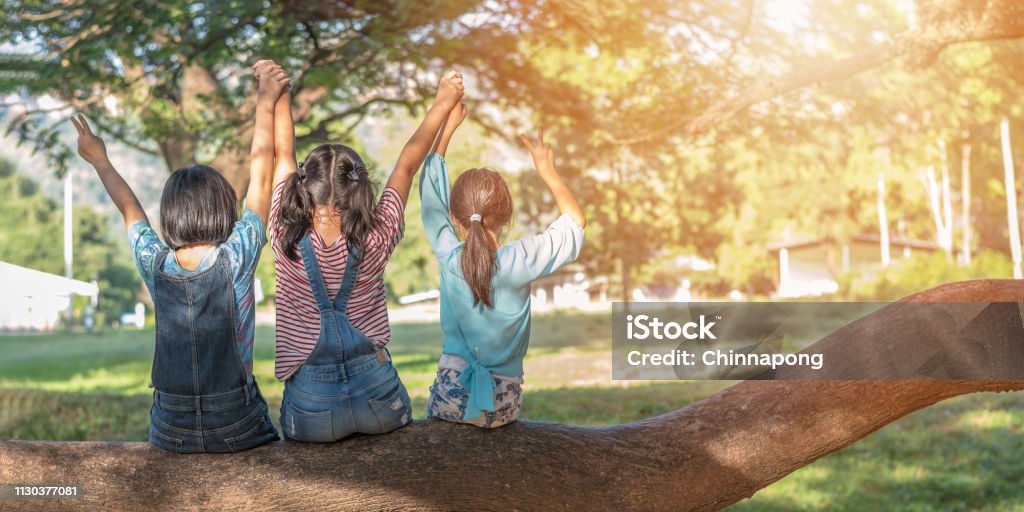 Children friendship concept with happy girl kids in the park having fun sitting under tree shade playing together enjoying good memory and moment of student lifestyle with friends in school time day Child Stock Photo