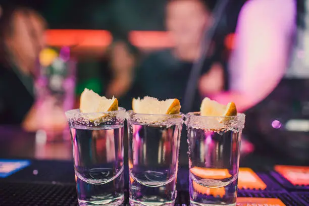 Photo of aperitif with friends in the bar, five glasses of alcohol with snacks lime and pistachio, salt and chili pepper for decoration. Tequila shots, vodka,whisky, rum. selective focus and copy space.