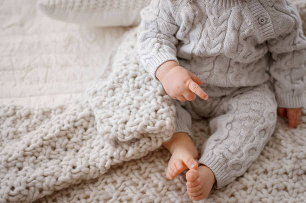 Baby Legs in Gray Cable Knit Romper Baby on a bed showing legs, arms, and bare feet, wearing a gray cable knit romper baby clothing stock pictures, royalty-free photos & images