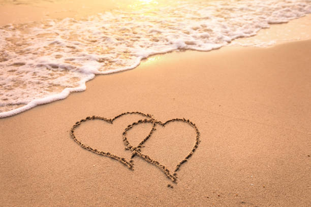 liebe romantische flitterwochen-urlaub oder zum valentinstag auf dem strand-konzept mit zwei herzen gezogen auf dem sand, tropischen kurzurlaub für paare, symbol - romantic getaway stock-fotos und bilder