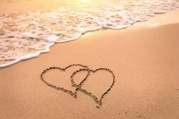 Photo of Romantic honeymoon holiday or Valentine's day on the beach concept with two hearts drawn on the sand, tropical getaway for couples, love symbol