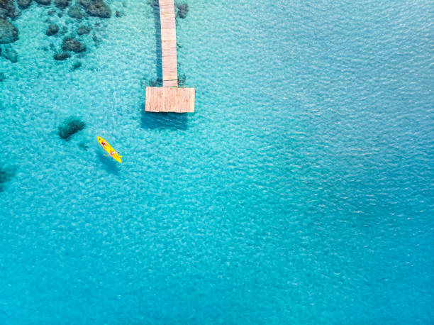 istock Tropical beach viewed from drone at beautiful vacation holidays destination with transparent turquoise sea water, pier and people kayaking. Top down aerial view of pristine island with copy space 1130402921