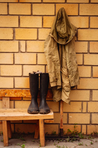 istock Farmers kit - rain coat haning on rake and rubber boots on a bench. 1130405113