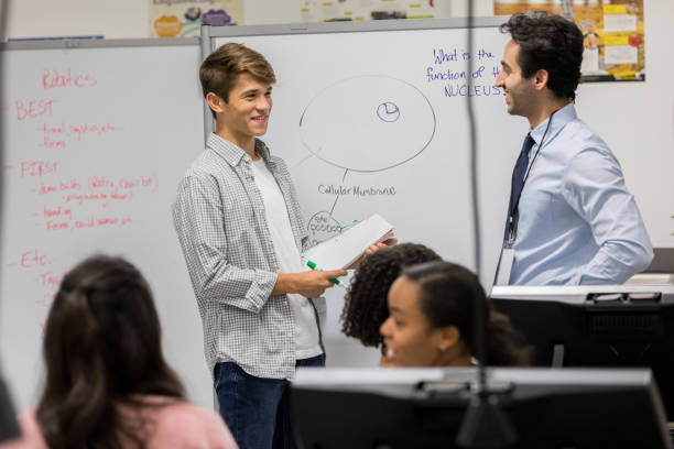 Teenage boy asks teacher a question Hispanic male high school student asks his science teacher a question during class. high school student classroom education student stock pictures, royalty-free photos & images