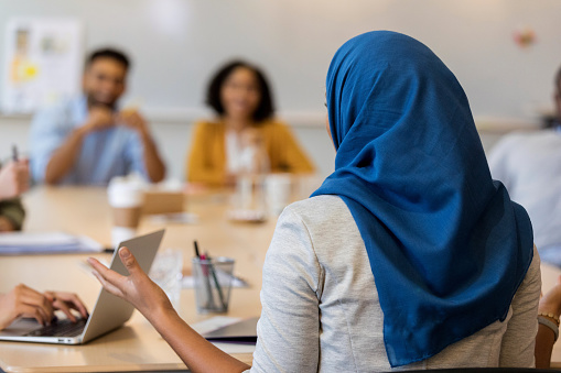 Rear view of confident female business manager in a hijab gestures while facilitating a staff meeting.