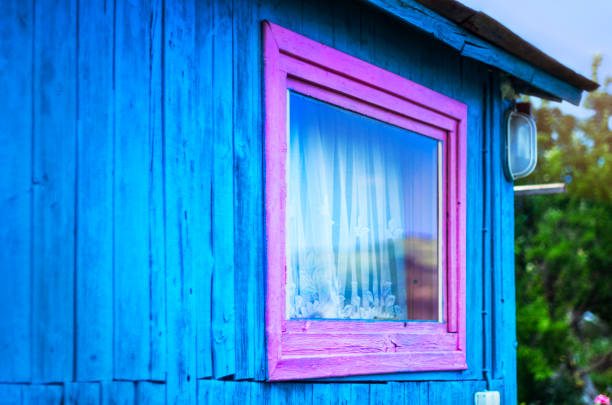 シンプルなデザイン コンセプト: 鮮やかな紫ウィンドウ フレーム、木製の板の青い壁に光。山の反射ガラス、白いカーテン。屋根庇。庭の木 - building exterior built structure old house ストックフォトと画像