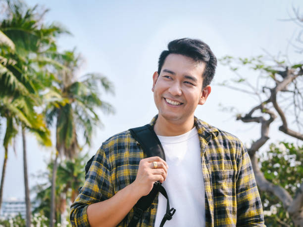 istock Asian man with backpack smiling at the beach with coconut tree background. 1130410502
