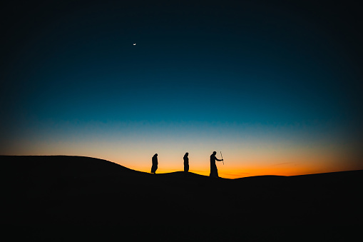 Árabes en las dunas de arena caminando unos detrás de otro durante el crepúsculo photo