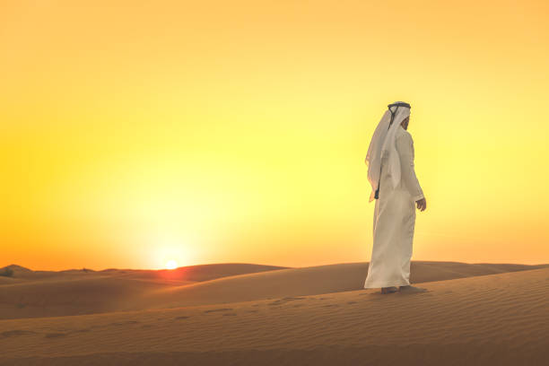 Arab man admiring expansive dunes during sunset Arab, Middle East, Sand Dunes, Desert, Tradition, Culture - Arab man standing on the sand dunes arabian desert stock pictures, royalty-free photos & images