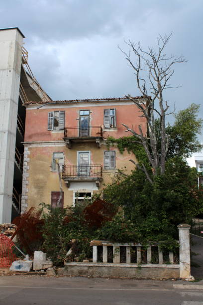 istock Apartment building abandoned by owners with destroyed doors and windows surrounded with tall dried tree and overgrown plants with construction material 1130421209
