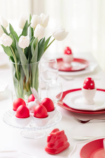 istock Happy easter. Decor and table setting of the Easter table is a vase with white tulips and dishes of red and white color. Easter colored eggs with white polka dots. 1130422383