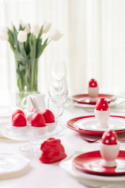 istock Happy easter. Decor and table setting of the Easter table is a vase with white tulips and dishes of red and white color. Easter colored eggs with white polka dots. 1130422386