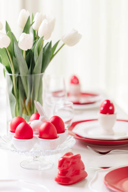 istock Happy easter. Decor and table setting of the Easter table is a vase with white tulips and dishes of red and white color. Easter colored eggs with white polka dots. 1130422388
