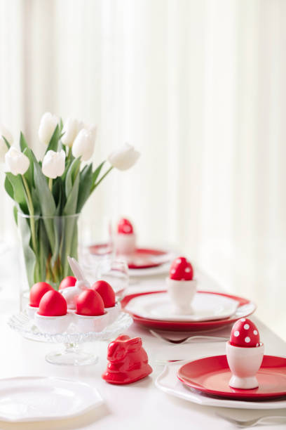 istock Happy easter. Decor and table setting of the Easter table is a vase with white tulips and dishes of red and white color. Easter colored eggs with white polka dots. 1130422394