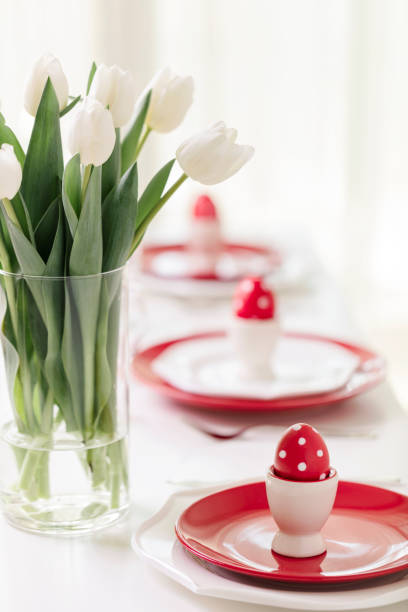 istock Happy easter. Decor and table setting of the Easter table is a vase with white tulips and dishes of red and white color. Easter colored eggs with white polka dots. 1130422404