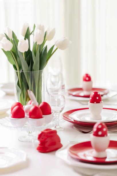 istock Happy easter. Decor and table setting of the Easter table is a vase with white tulips and dishes of red and white color. Easter colored eggs with white polka dots. 1130422412