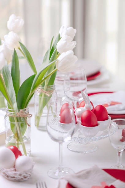 istock Happy easter. Decor and table setting of the Easter table is a vase with white tulips and dishes of red and white color. Easter colored eggs with white polka dots. 1130422432