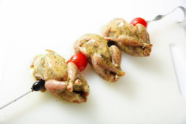 The raw carcass of a quail for the grill on the skewer on a light background.