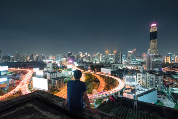 남자는 밤에 빛나는 도시를 관광 하는 발코니에 앉아 있다 - bangkok night thailand traffic 뉴스 사진 이미지