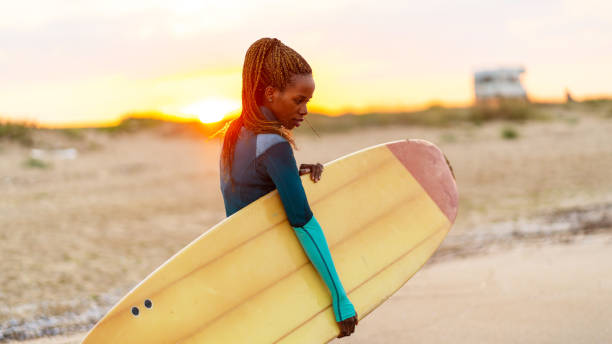 istock African woman holding surfboard and walking on beach 1130440620