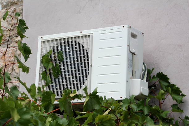 istock Wall mounted outside air conditioner AC unit mounted on cracked back wall with stone tiles part of family house in front of dense garden vine plants 1130441461