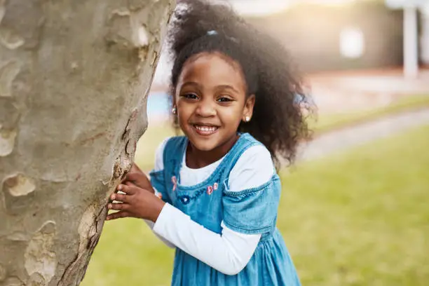 Portrait of an adorable little girl playing at a tree outdoors