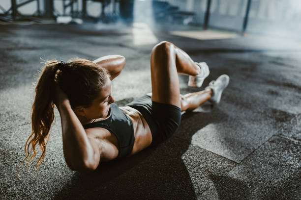 Athletic woman exercising sit-ups in a health club. Young female athlete exercising sit-ups with hands behind her head in a gym. abdominal muscle stock pictures, royalty-free photos & images