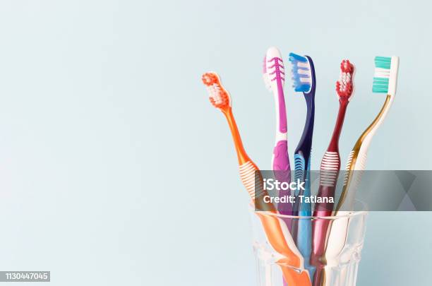 Multigekleurde Tandenborstels In Een Glazen Beker Blauwe Achtergrond Stockfoto en meer beelden van Tandenborstel