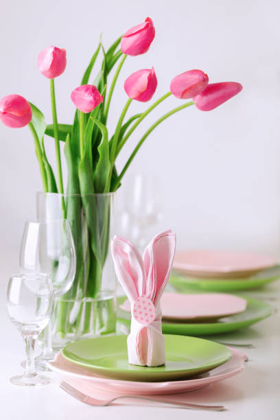 Happy easter. Decor and table setting of the Easter table is a vase with pink tulips and dishes of pink and green color. Selective focus.