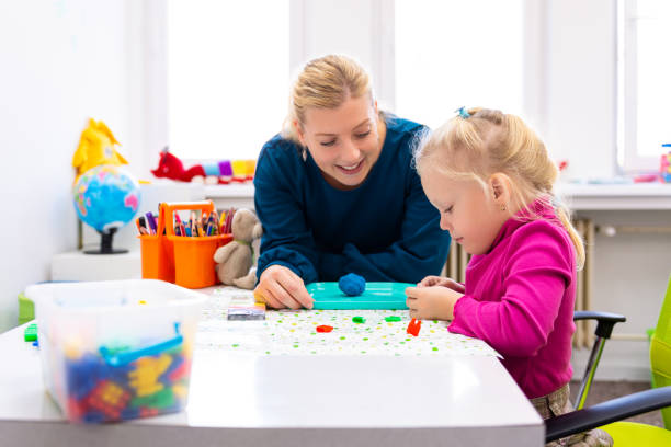 Toddler girl in child occupational therapy session doing sensory playful exercises with her therapist. stock photo