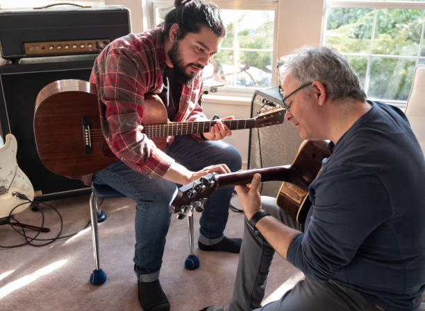 giovane ispanico che insegna all'uomo caucasico maturo a suonare la chitarra - music lessons foto e immagini stock