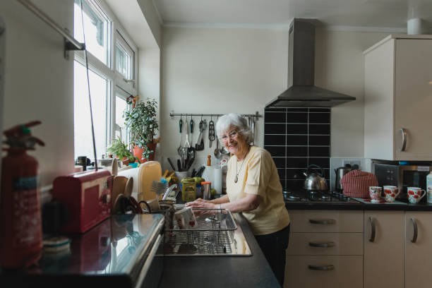 femme âgée heureuse de lavage des plats - senior adult independence lifestyles home interior photos et images de collection