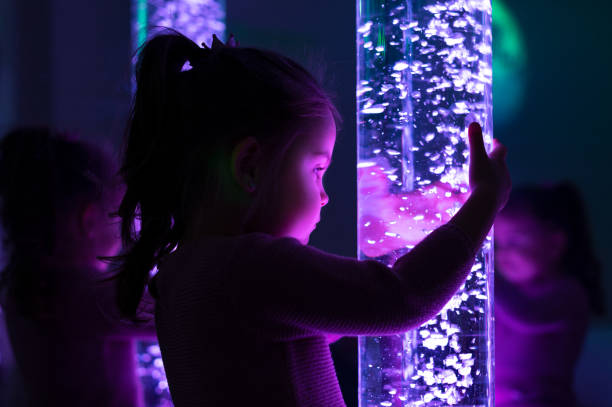 Child in therapy sensory stimulating room, snoezelen. Child interacting with colored lights bubble tube lamp during therapy session. stock photo
