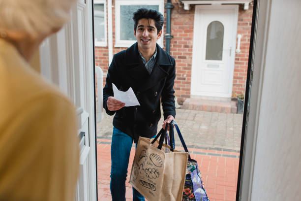 Delivering Groceries to an Elderly Woman Teenage boy is delivering a bag of shopping to an elderly woman at home. two-white-doors stock pictures, royalty-free photos & images